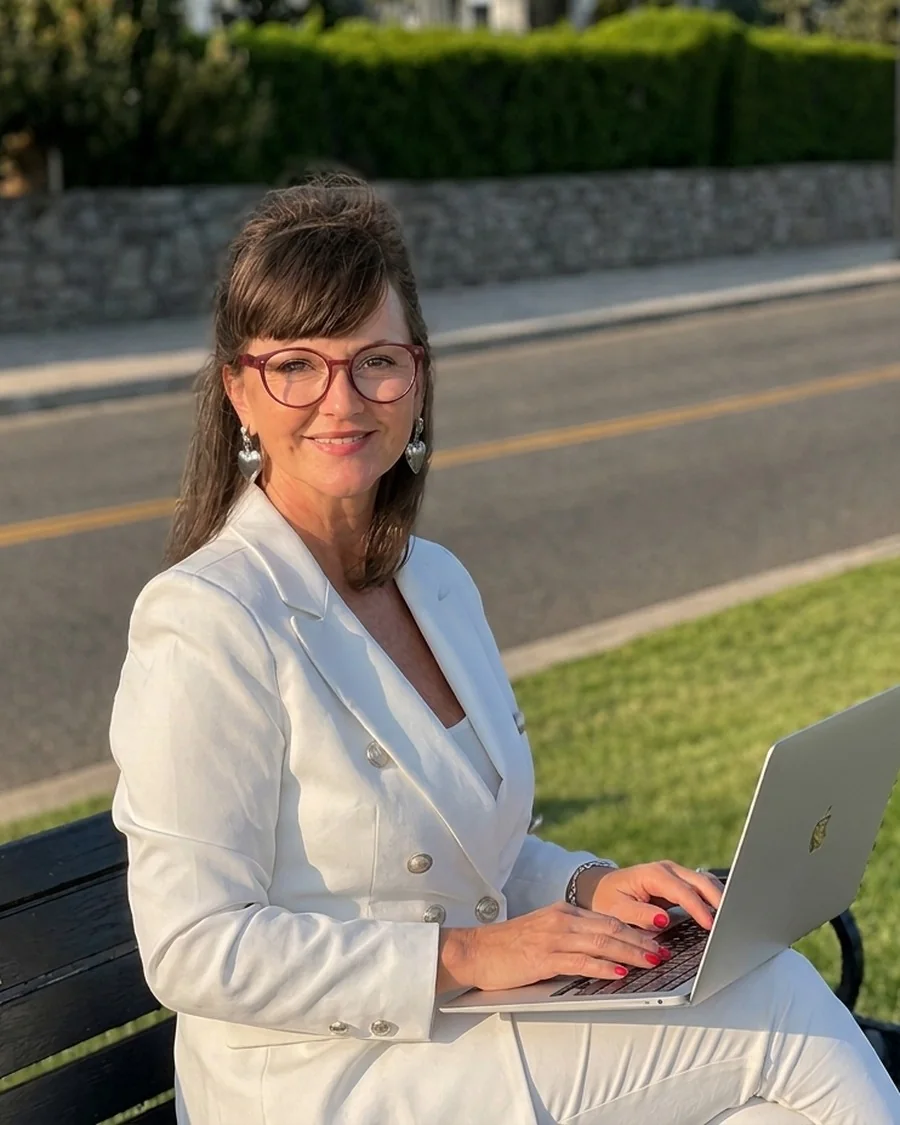 Maida White of Bonbonica working on a laptop on a bench in Swampscott, Massachusetts, with the road and grass behind her